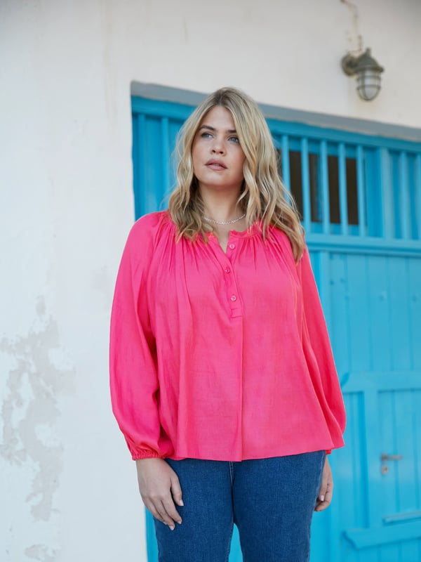 In striking pink, this blouse is cut from a soft chambray fabric thats so comfortable to wear. It has a round neckline with soft gathers, and a button-through front that creates a lengthening effect. Long raglan sleeves with elasticated cuffs add comfort and coverage, and complement its slightly swingy shape beautifully.