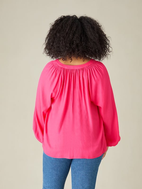 In striking pink, this blouse is cut from a soft chambray fabric thats so comfortable to wear. It has a round neckline with soft gathers, and a button-through front that creates a lengthening effect. Long raglan sleeves with elasticated cuffs add comfort and coverage, and complement its slightly swingy shape beautifully.
