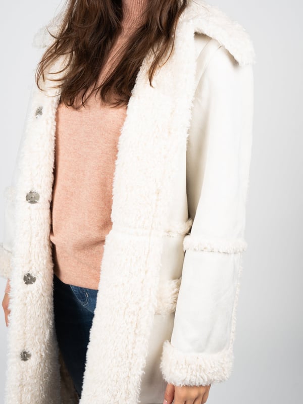 De jas van imitatiebont is de perfecte combinatie van elegantie en comfort, geschikt voor elke situatie, ongeacht de gelegenheid.

De uniforme kleur van de jas maakt hem extreem veelzijdig en makkelijk te combineren met verschillende stijlen, van casual tot meer formeel.

Grote metalen knopen met een merkelement geven de jas een uniek karakter en benadrukken de hoge kwaliteit en aandacht voor detail.

Diepe zakken aan de voorkant voegen niet alleen functionaliteit toe door het opbergen van noodzakelijke kleine items, maar zorgen ook voor extra comfort en warmte op koelere dagen.