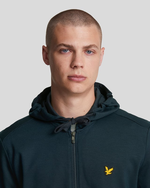 Ervaar comfort en stijl met de Lyle &amp; Scott Full Zip Dark Navy Hoodie. Gemaakt van 100% zacht katoen, biedt deze hoodie een ademende en comfortabele pasvorm, perfect voor dagelijks gebruik. De volledige ritssluiting maakt het gemakkelijk om te dragen in laagjes, terwijl de twee voorzakken handige opbergruimte bieden voor je essentials of een plek om je handen te warmen. De donkerblauwe tint zorgt voor een tijdloze look die moeiteloos bij elke outfit past. Of je nu een casual dagje uitgaat of thuis ontspant, deze hoodie combineert functionaliteit met klassieke stijl om je de hele dag comfortabel en zelfverzekerd te houden