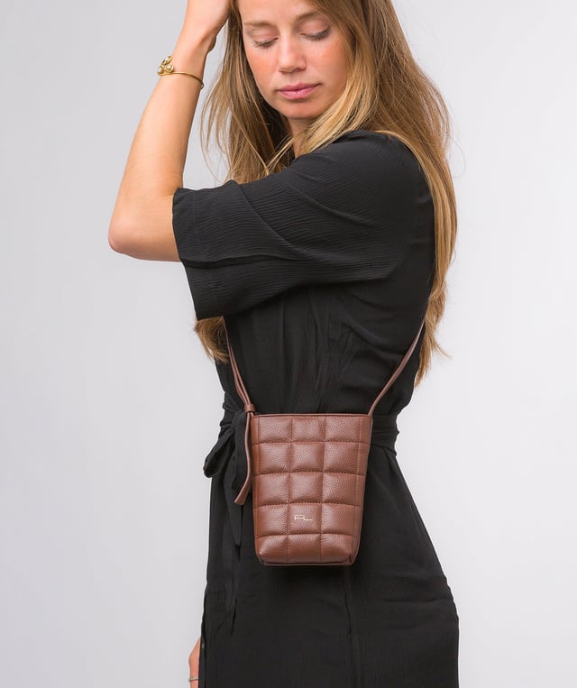 The 'Elouise' cross body phone bag from the Pure Luxuries Marylebone collection is handcrafted from high-quality, genuine Nappa leather with a natural super-soft touch. The eye-catching quilted design on the front gives the bag a unique silhouette, along with extra protection. A concealed magnetic closure keeps the contents of the bag secure. The interior is lined with 100% cotton and includes a slip pocket and two card slots. Comes with a matching and adjustable slim leather strap with a maximum drop length of 65cm. The minimalist Pure Luxuries logo is embossed in gold foil for a beautifully simple finishing touch.