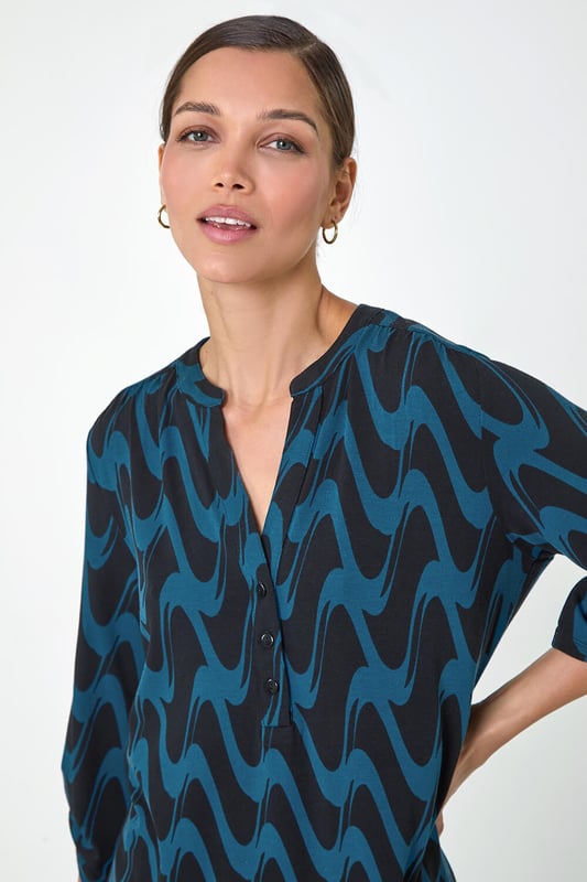 Geometric Print Stretch Blouse from Roman. Elevate your wardrobe this season with our stunning abstract blouse. The bold print and woven silhouette make it versatile for any occasion. The notch neckline, adjustable 3/4 length sleeves and front button details adds a touch of sophistication. Pair it with black jeans and boots for a daytime look or add tailored trousers perfect for those desk-to-dinner days