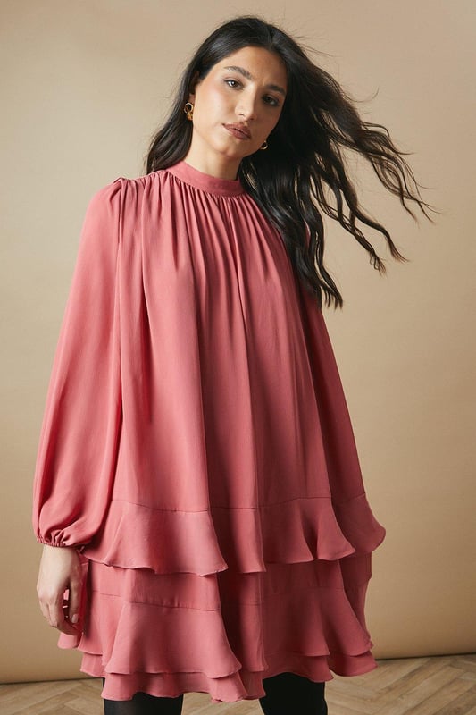 Elegant high neck design for a sophisticated look
        Flowy chiffon fabric creates a graceful silhouette
        Voluminous balloon sleeves add a romantic touch
        Tiered ruffle hem for playful movement
        Versatile mini length suitable for various occasions
    
    This charming high neck chiffon mini dress from Oasis is the epitome of feminine allure. The airy chiffon fabric drapes beautifully, creating a flattering and comfortable fit for all-day wear. The dress features eye-catching balloon sleeves that add a touch of drama to your ensemble, while the tiered ruffle hem introduces a playful element to the overall design. Perfect for casual daytime events, this dress can be styled effortlessly for family gatherings or weekend brunches. Pair it with ankle boots and a leather jacket for an edgy contrast, or opt for ballet flats and delicate jewellery for a softer look. The versatile nature of this dress allows for easy transition from day to night - simply swap your accessories to suit the occasion. Embrace your girly side and make a statement in this delightful Oasis creation.