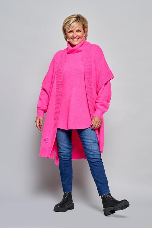 Der Burnaby-Cardigan in einem auffälligen Rosaton ist perfekt für einen eleganten und bequemen Look. Dieser Cardigan verfügt über eine einzigartige Stickerei, die eine persönliche Geschichte erzählt, inspiriert von Carolines Tattoo. Die Tauben symbolisieren ewige Liebe. Der Cardigan hat einen weichen Schalkragen aus Rippstoff, breite Rippbündchen und kurze Ärmel. Die gerade Passform, die bis zum Knie reicht, bietet sowohl Stil als auch Komfort. Dieser übergroße Cardigan besteht aus einer Mischung aus 30 % Polyester, 27 % Nylon, 25 % Acryl, 15 % Wolle und 3 % Elastan und ist leicht, weich und atmungsaktiv, sodass er für jede Jahreszeit geeignet ist. Die leuchtend rosa Farbe der Strickjacke erleichtert die Kombination mit anderen Kleidungsstücken. Für einen femininen Look können Sie die Strickjacke mit der weißen Winslow-Bluse tragen. Der Burnaby-Cardigan mit kurzen Ärmeln und offenem Tragestil lässt sich ideal über dem Brampton-Pullover für einen winterlichen Look tragen. Entdecken Sie die Vielseitigkeit und den stilvollen Charakter dieser Kombinationen.