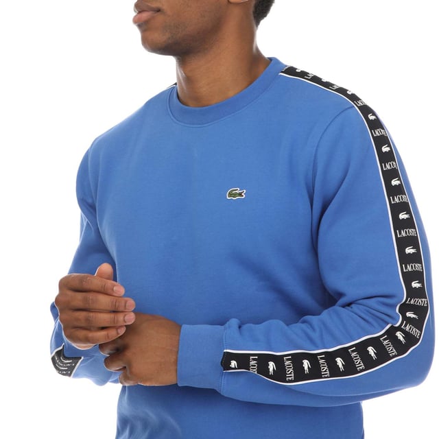 Mens Lacoste Logo Stripe Jogger Sweatshirt in blue.- Ribbed crewneck.- Elasticated cuffs and hem.- Embroidered logo on the chest and a logo pattern down both sleeves.- Classic fit.- Shell Fabric: 80% Cotton  20% Polyester. Rib edge: 98% Cotton  2% Elastane.- Ref: SH749200IXV
