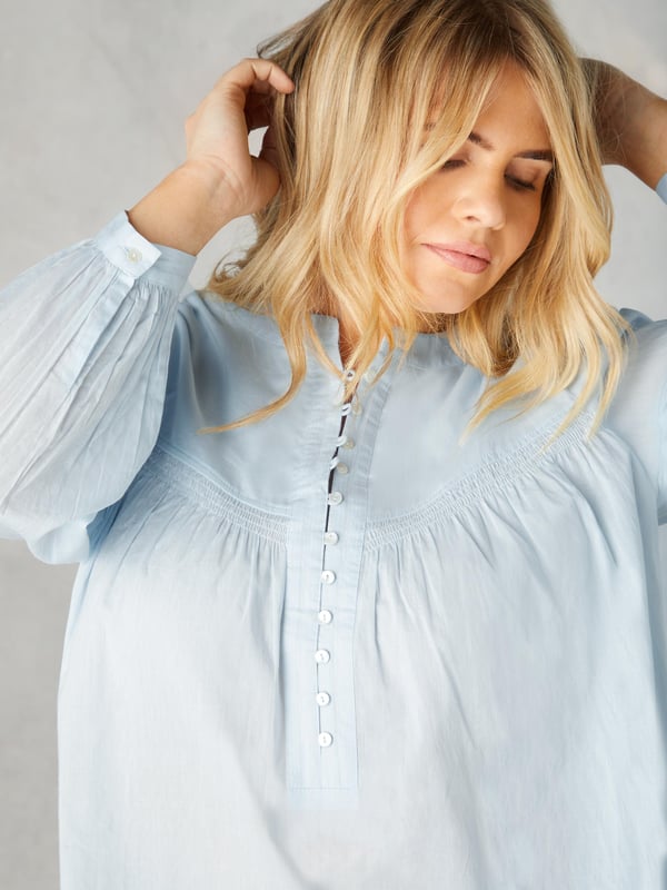 In classic blue, this blouse is cut from the softest of cottons. With a nehru collar, it has a button-up front placket with pretty rouleau buttons, as well as shirring detail at the yoke. Full-length sleeves with button up cuffs create an elegant silhouette, especially when combined with its high-low hem which provides that all-important coverage.