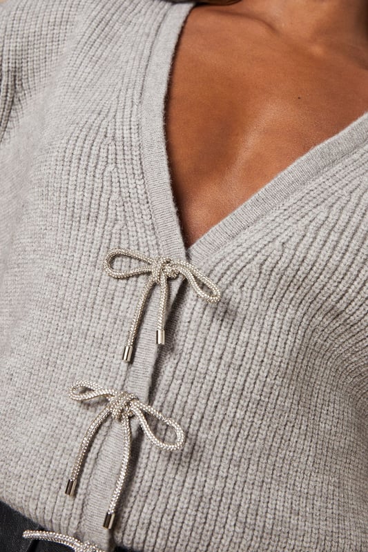 Elegant V-neck design for a flattering neckline
        Charming crystal bow buttons add a touch of sparkle
        Ribbed knit texture for added visual interest
        Versatile cropped length perfect for layering
        Long sleeves for warmth and style
    
    Embrace feminine charm with this Crystal Bow Button Down Jumper from Oasis. The delicate crystal bow buttons lend a touch of whimsy to this otherwise classic piece, making it a versatile addition to your wardrobe. Style it with a pleated skirt and opaque tights for a chic daytime look, or pair it with tailored trousers for a more polished ensemble. The cropped length works wonderfully with high-waisted bottoms, creating a balanced silhouette. For casual outings, throw it over a floral dress and add ankle boots for an effortlessly stylish look. This jumper is perfect for family gatherings, brunch dates, or casual Fridays at the office. Its soft knit fabric ensures comfort, while the ribbed texture adds a subtle sophistication to your outfit.