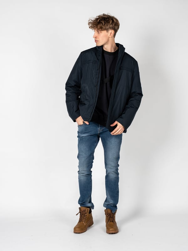Un diseño sencillo es la solución perfecta para aquellos que valoran la clásica y el minimalismo, al mismo tiempo que desean verse estilosos y elegantes en cualquier situación.

El cuello alto añade un carácter moderno al conjunto, a la vez que ofrece protección adicional contra el viento y el frío, lo que hace que esta prenda sea una excelente elección para las condiciones meteorológicas cambiantes.

Con una capucha oculta en el cuello, puedes estar preparado para las lluvias inesperadas, y su ingenioso diseño permite que se guarde fácilmente cuando no es necesaria, manteniendo un aspecto elegante.

Se abrocha con una cremallera logotipada y botones a presión, lo que no solo añade un estilo único, sino que también proporciona protección adicional contra el frío, destacando al mismo tiempo la atención a los detalles.

En el frente, cuatro bolsillos, dos con cremallera y dos con botones a presión, ofrecen mucho espacio para guardar los artículos esenciales y su variedad permite una mejor organización.

En la manga izquierda, un detalle de la marca constituye un sutil, pero claro refuerzo del prestigio de la marca, agregando un carácter exclusivo a la prenda y distinguiéndola de las demás.

Fabricada con tela de alta calidad, transpirable y resistente al agua, lo que garantiza no solo comodidad al usarla, sino también protección contra las condiciones atmosféricas adversas, haciendo que sea una elección ideal para cualquier época del año.