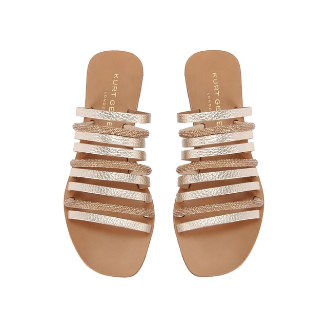 The Kurt Geiger Daisy Flat Sandal is a slip-on sandal. There are multiple gold straps across the upper each with its own metallic finish or crystal embellishment.