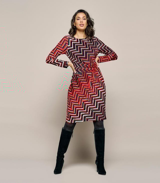 Ontdek de Mart Visser jersey print jurk, genaamd de Eloise. Deze jurk belichaamt stijl en comfort perfect. Het is een echte aanrader vanwege de opvallende contrastrijke print en de kreukvrije jerseykwaliteit die zijdezacht aanvoelt. De stof is bedrukt met een grafische en kleurrijke zigzagprint in rood, wit en zwart, wat een uniek en flatterend effect creëert. De damesjurk biedt heerlijk draagcomfort dankzij de mix van elastaan en polyester, waardoor je je vrij kunt bewegen. De gedrapeerde tailleband flatteert perfect rondom de buik en heupen. Deze knielange jurk heeft een voering met een fijne stretch, sluit met een blinde ritssluiting aan de achterzijde en heeft lange mouwen. Geschikt voor zowel feestelijke als zakelijke gelegenheden. Maak je vrouwelijke en moderne look compleet met een zwart jack en elegante hakken! Ontdek ook de Caitlin print top met dezelfde opvallende print.