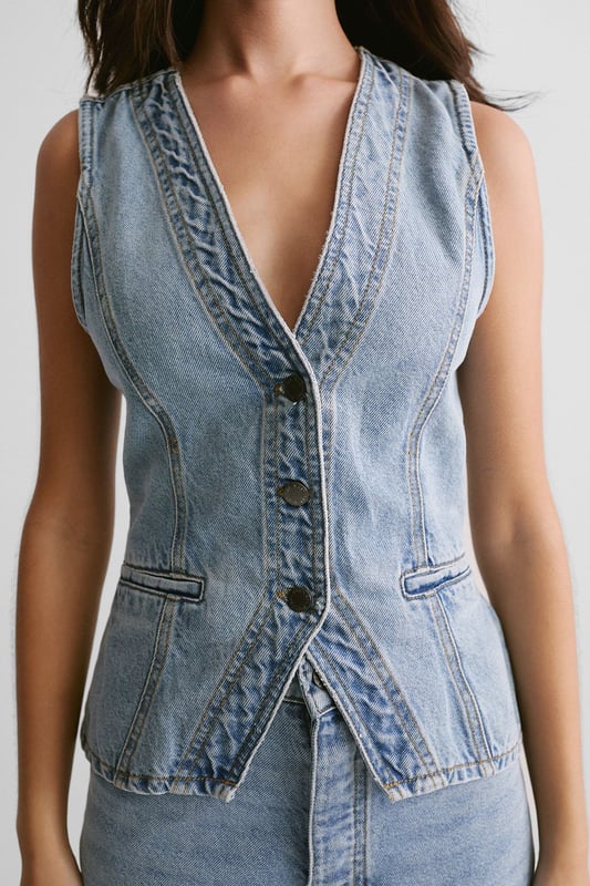 Sleek longline silhouette for a contemporary twist on classic denim
        Plunging V-neckline adds a touch of allure
        Button-front closure for easy wear and versatile styling
        Fitted waist with adjustable belt detail for a customised fit
        Crafted from sturdy denim fabric for long-lasting wear
    
    The Longline Denim Waistcoat from NastyGal is a versatile piece that seamlessly blends casual cool with a hint of sophistication. This sleeveless wonder can be styled in myriad ways to suit various occasions. For a laid-back daytime look, pair it with wide-leg jeans and trainers, as seen on our model. Layer it over a crisp white shirt and tailored trousers for a smart-casual ensemble perfect for family gatherings or informal work events. The adjustable belt allows you to cinch in the waist for a more defined silhouette, while the longline cut provides flattering coverage. Whether worn open as a vest or buttoned up as a standalone top, this denim waistcoat is sure to become a staple in your wardrobe, offering endless styling possibilities for the fashion-forward individual.