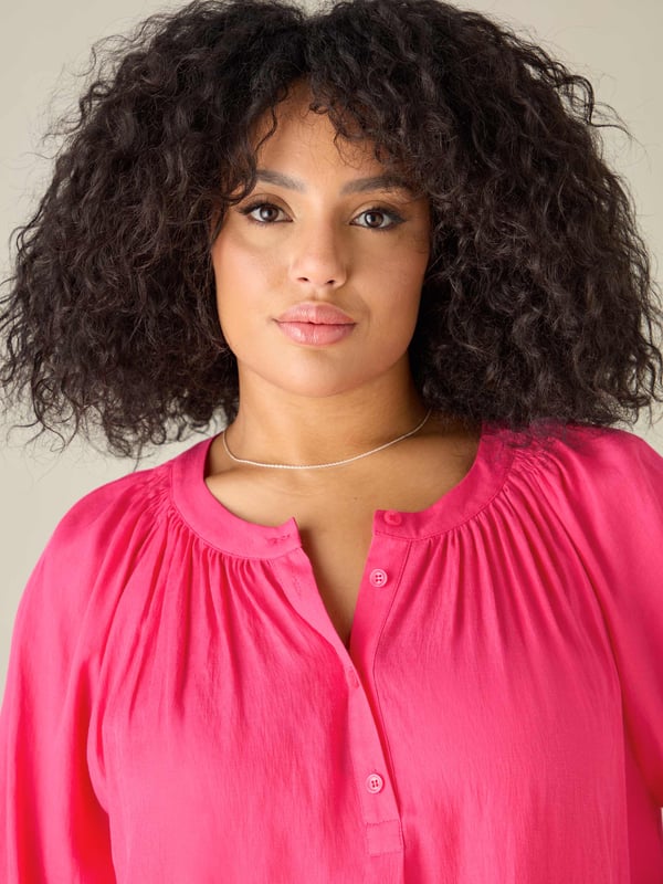 In striking pink, this blouse is cut from a soft chambray fabric thats so comfortable to wear. It has a round neckline with soft gathers, and a button-through front that creates a lengthening effect. Long raglan sleeves with elasticated cuffs add comfort and coverage, and complement its slightly swingy shape beautifully.