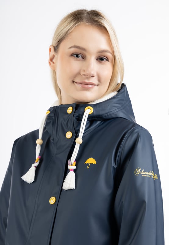 Die mit Webpelz gefütterte Regenjacke von Schmuddelwedda ist die perfekte Antwort auf Kälte und Nässe. Ihr Obermaterial ist beschichtet und alle Nähte sind komplett versiegelt, was dem trendigen Friesennerz eine Funktionalität beschert, die sich bei Wind und Wetter bewährt hat. Für wohlige Wärme sorgt ein Innenfutter aus weichem Webpelz, das sich auch in der Kapuze wiederfindet. Apropos Kapuze: Die schicke Kordel mit bunten Enden und Quasten ist ebenso ein Eyecatcher wie die aufwendig geprägten Accessoires. Der für Schmuddelwedda typische Regenschirm-Print ziert die Brust, der Markenname den Oberarm.  Regenjacke mit Webpelzfutter