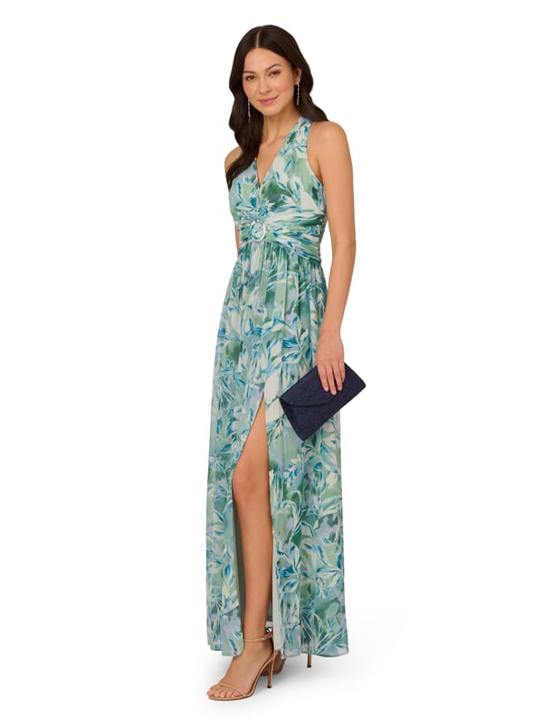 Pretty little details make this halter gown shine. This formal dress features a faux wrap bodice with halter neckline, shirred detailing at the waist surrounding a fabric-trimmed ring at the centre, and a flowing skirt with thigh-high slit. Fully lined, this dress is crafted from leaf-printed chiffon with shirred detailing through the skirt. A zipper closure at the centre back completes this evening gown. A pretty look for day or nighttime events, style this dress with nude heels and a sparkling clutch.
