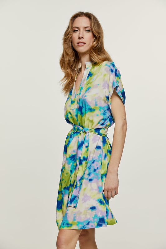 Deze zomerjurk met print is gemaakt van geweven viscose. Het is mouwloos en heeft een boord bij de armsgaten in dezelfde stof. Het heeft een mandarijnkraag van 2 cm en een sluiting van 4 cm bij de halslijn aan de voorkant om een V-vorm te creëren. Aan elke kant zit een binnenzak.  De jurk heeft grote splitten van 20 cm aan elke kant. De jurk kan worden gedragen met de riem of zonder als u een meer ontspannen zakjurkstijl wilt creëren. De riem in dezelfde stof is inbegrepen. Dit kledingstuk is gestileerd in een recht los silhouet.