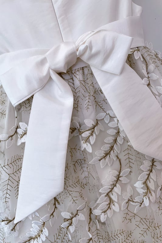 Another new style for us this year. We are so excited to have sourced the beautiful fabric for this style LUCY.

Fern style embroidered leaves in ivory, attached by gold thread stems. The gold catches in the light as the skirt moves and has a 3D effect which makes the leaves look realistic. A very distinctive fabric makes this girls special occasion dress quite unique. You won't see another dress like this on the high street!

The top of the dress is made using our 'Mock Silk' fabric and has a pin tucked sash that ties at the back in a big bow. It's fully lined in lightweight soft 100% cotton, just in case your little one has sentitive skin and also helps them not to get too sweaty after all the twirling and pirouetting around. Let's be honest ... all girls will feel like a princess in this!

All our dresses arrive with you on a satin padded hanger to help keep the dress in the best shape and then protected by one of our heritage garment keepsake bags
Outer - 100% Polyester
Lining - 100% Cotton
Dry Clean or Hand Wash only