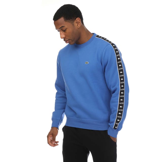 Mens Lacoste Logo Stripe Jogger Sweatshirt in blue.- Ribbed crewneck.- Elasticated cuffs and hem.- Embroidered logo on the chest and a logo pattern down both sleeves.- Classic fit.- Shell Fabric: 80% Cotton  20% Polyester. Rib edge: 98% Cotton  2% Elastane.- Ref: SH749200IXV