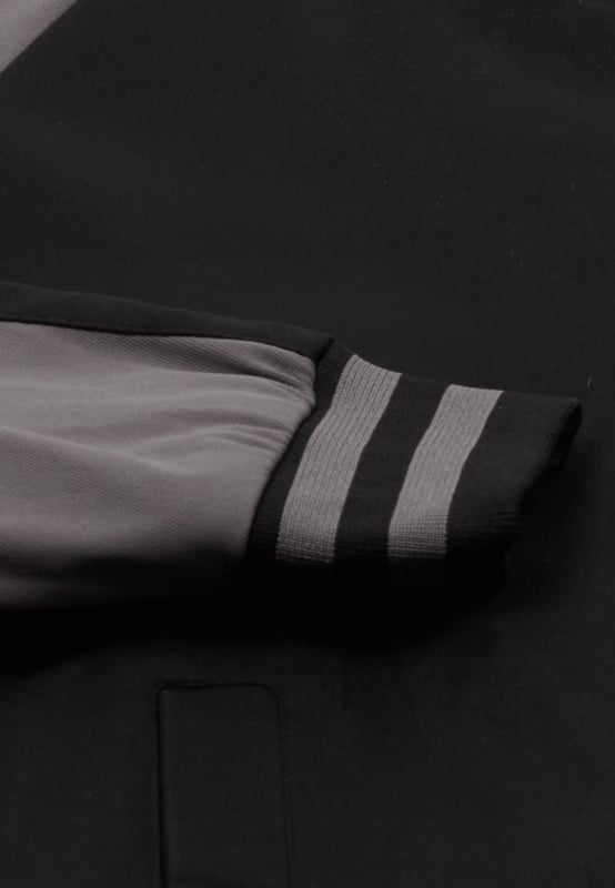 Dit jack heeft een klassieke varsity-stijl en heeft een geribde kraag, versierd met een gestreept patroon en vastgezet met drukknopen. De lange mouwen hebben een contrasterend ontwerp op de schouders en bovenarmen, aangevuld met geribde en gestreepte manchetten die passen bij de kraag. Paspelzakken op heuphoogte zorgen voor functionaliteit, terwijl de geribde zoom naadloos overgaat in de algehele sportieve look die doet denken aan Amerikaanse universiteitsmode.  Jas