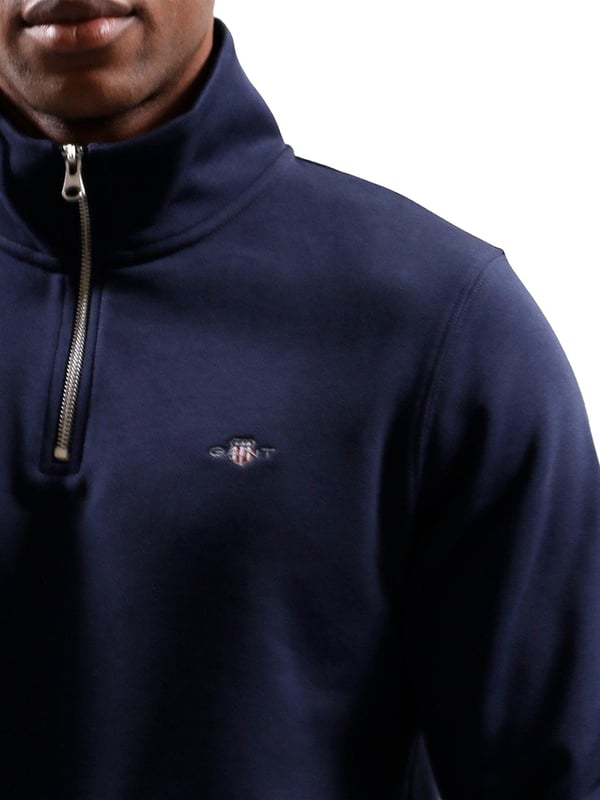 This versatile half-zip sweatshirt combines comfort and style with a premium cotton-polyester blend that's perfect for transitional weather. Featuring a small, intricately embroidered GANT graphic on the chest, it showcases a subtle yet elevated design. The ribbed hem and cuffs create a tailored silhouette. Designed for a regular fit, the half-zip collar adds a touch of sporty elegance, while the durable fabric ensures long-lasting wear.