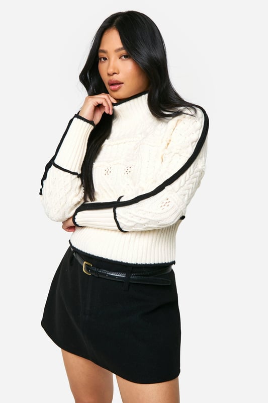 High neck design for a chic, sophisticated look
        Intricate cable knit pattern adds texture and visual interest
        Contrasting trim detail along sleeves and body for a striking effect
        Cropped length perfect for pairing with high-waisted bottoms
        Petite fit tailored for smaller frames
    
    Make a statement in this eye-catching petite cable knit jumper. The high neck design and contrasting trim details create a bold, contemporary look that's perfect for the fashion-forward woman. Style this versatile piece for a range of casual occasions, from coffee dates to family gatherings. Pair it with a high-waisted mini skirt and chunky loafers for a trendy daytime ensemble, or dress it up with tailored trousers and ankle boots for a smart-casual evening look. The cropped length is ideal for showing off your favourite bottoms, while the petite fit ensures a flattering silhouette for smaller frames. Add a leather jacket for extra edge, or keep it simple with minimalist accessories to let the jumper's unique design shine. This Boohoo piece is a must-have addition to your autumn-winter wardrobe, offering both style and comfort for the fashion-conscious woman.
