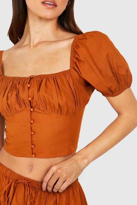Plunging square neckline for a daring look
        Puff sleeves add a romantic touch
        Button-down front detail for adjustable styling
        Cropped length to showcase your midriff
        Fitted waist creates a flattering silhouette
    
    Make a statement in this eye-catching crop top that combines vintage charm with modern flair. The plunging neckline and puff sleeves create a captivating contrast, perfect for those looking to turn heads on a night out. Pair it with the matching high-waisted skirt for a coordinated ensemble that's sure to impress at your next social gathering. For a more casual look, team it with high-waisted jeans and trainers. The versatile design allows for easy transition from day to night - simply swap your footwear and add some bold jewellery to elevate your outfit for evening drinks or dancing. This Boohoo piece is ideal for the fashion-forward woman who isn't afraid to showcase her style and confidence.