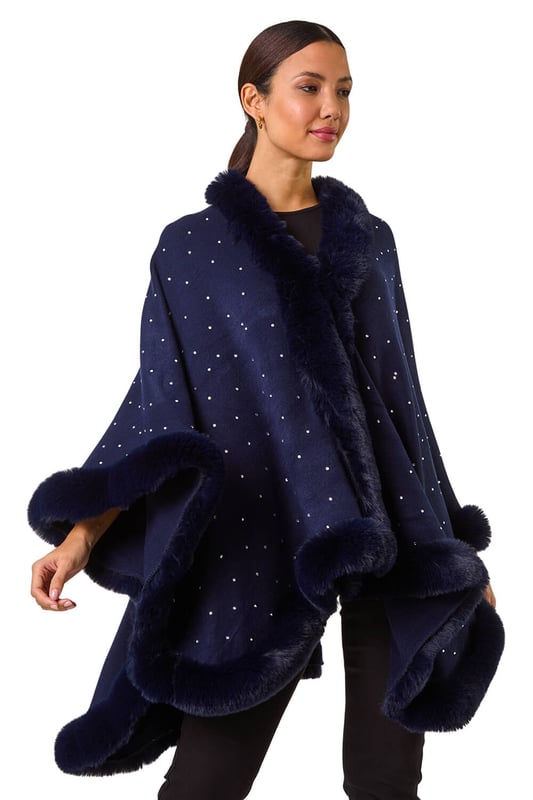 Hotfix Faux Fur Trim Cape from Roman. This style is ONE size.  Wrap up in style this Autumn and Winter with this all over hotfix faux fur trim cape. In a classic black hue with dazzling silver hotfix detailing, this cosy cape is the perfect layering piece. Simply throw on over a t-shirt and jeans for an effortlessly chic and stylish look.
