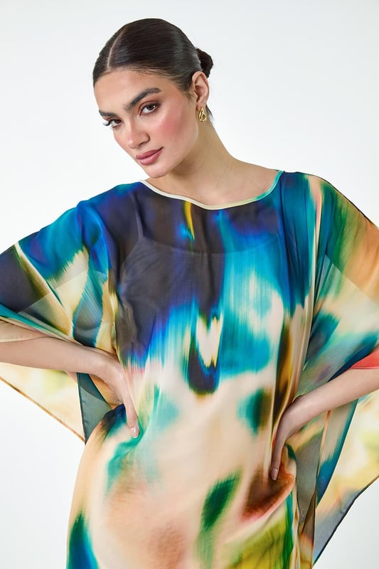 Abstract Print Chiffon Draped Tunic Dress from Roman. Add a touch of elegance to your wardrobe with this Ariella chiffon draped tunic dress. The round neckline and abstract print are complemented by the floaty chiffon draping, creating a flattering dipped hem and cape-style sleeves for a chic look. The stretch jersey inner slip dress lining ensures all-day comfort, while the knee length and adjustable straps in the lining add extra versatility to this piece. Perfect for those Summer wedding invitations, pair with strappy heels and a clutch bag for your next special occasion!