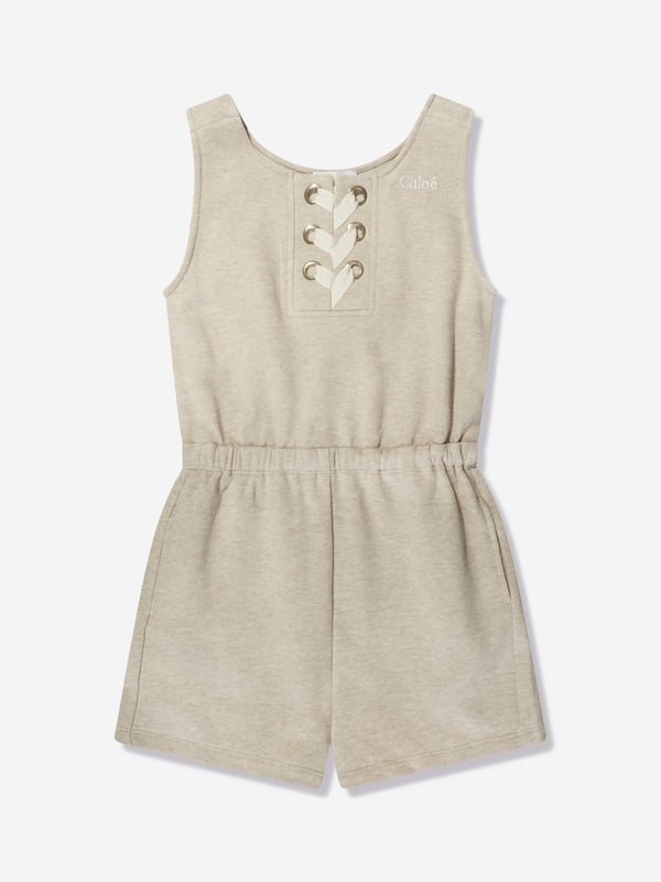 Chloé Girls Sleeveless Playsuit in Beige Chloé portray demure whimsical subjects in their exquisite aesthetics. This girls sleeveless jumpsuit is depicted in unbrushed fleece cotton via lacing at the front, golden trims, large embroidery Chloé on the chest, elasticated waist and piped pockets. She will look and feel divine. 100% Organic Cotton Sustainable