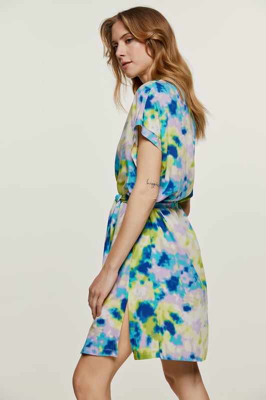Deze zomerjurk met print is gemaakt van geweven viscose. Het is mouwloos en heeft een boord bij de armsgaten in dezelfde stof. Het heeft een mandarijnkraag van 2 cm en een sluiting van 4 cm bij de halslijn aan de voorkant om een V-vorm te creëren. Aan elke kant zit een binnenzak.  De jurk heeft grote splitten van 20 cm aan elke kant. De jurk kan worden gedragen met de riem of zonder als u een meer ontspannen zakjurkstijl wilt creëren. De riem in dezelfde stof is inbegrepen. Dit kledingstuk is gestileerd in een recht los silhouet.