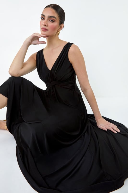 Plain Knot Front Maxi Dress from Roman. Turn heads in this luxuriously elegant knot front maxi dress. This exquisite sleeveless dress features a flattering v-neckline and a striking v-back detail, ensuring you make a sophisticated statement. With a fit and flare silhouette, this plain dress is fitted at the waist and flows into a floor-sweeping length, perfect for special occasions. The stretch jersey fabric drapes beautifully, while the knot detail at the waist adds an extra touch of glamour. Whether you're attending a wedding reception or a formal dinner, pair with strappy heels and a fascinator for a Summer wedding look.