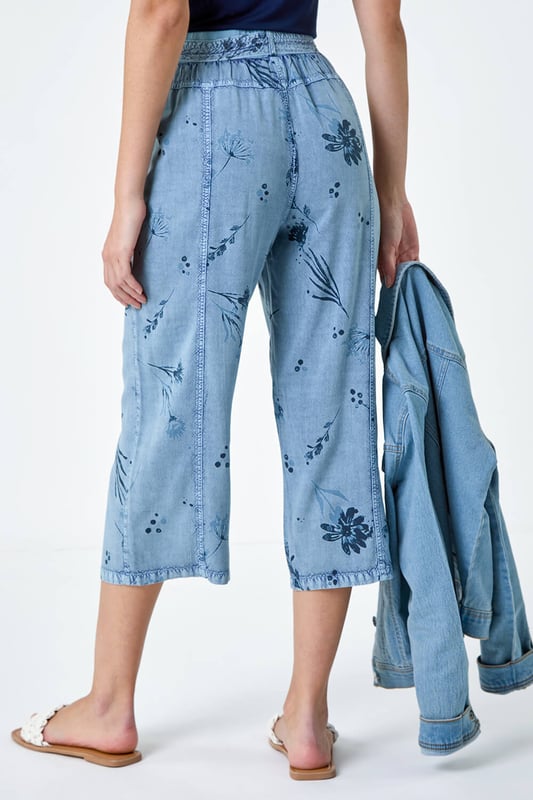 Floral Print Culotte Trousers from Roman. Add a touch of floral flair to your Spring wardrobe with these stylish culotte trousers. Featuring a cute floral print on a denim wash backdrop, these trousers are perfect for the new season. The elasticated waist with a tie belt detail offers both comfort and style, while the cropped culotte length and wide leg shape create a flattering silhouette. The light woven material and pull-on design make them a real Spring staple. Complete your look with a denim jacket, cami top and sandals for effortless daywear.