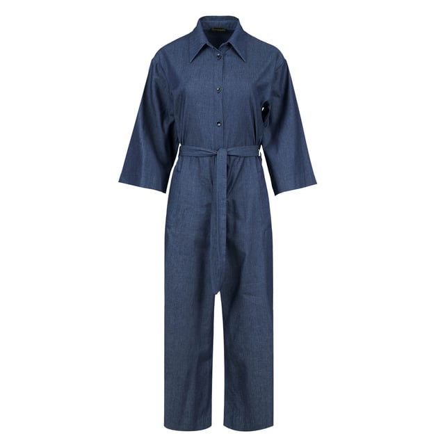 Deze indigo jumpsuit is gemaakt van katoen. Het heeft ¾ mouwen en een kraag. Er is een halssluiting met zwarte plastic knopen. Er zijn zakken aan de zijkanten met elk een riemlus. Het heeft een 3 cm brede ceintuur van dezelfde stof die door twee ceintuurlussen in de taille loopt. Aan de achterkant zit een omgekeerde plooi. De jumpsuit heeft een beenlengte van 7/8.
