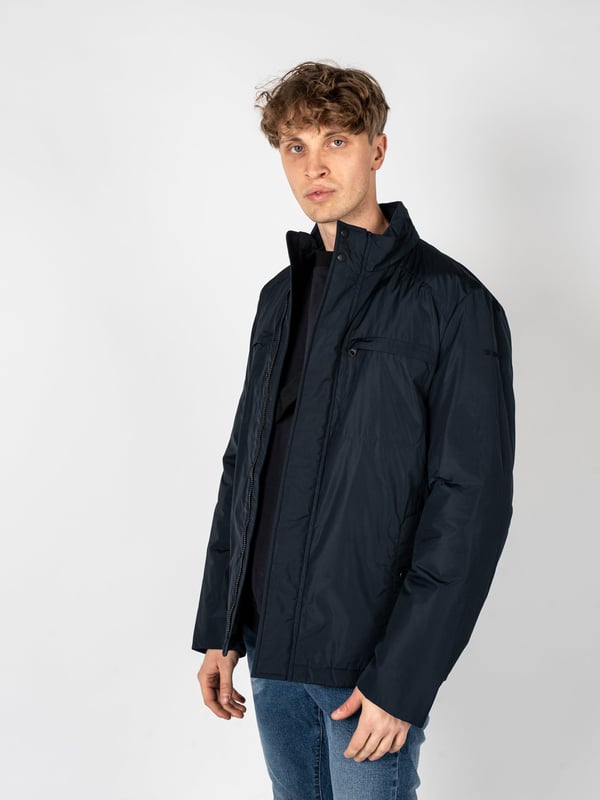 Un diseño sencillo es la solución perfecta para aquellos que valoran la clásica y el minimalismo, al mismo tiempo que desean verse estilosos y elegantes en cualquier situación.

El cuello alto añade un carácter moderno al conjunto, a la vez que ofrece protección adicional contra el viento y el frío, lo que hace que esta prenda sea una excelente elección para las condiciones meteorológicas cambiantes.

Con una capucha oculta en el cuello, puedes estar preparado para las lluvias inesperadas, y su ingenioso diseño permite que se guarde fácilmente cuando no es necesaria, manteniendo un aspecto elegante.

Se abrocha con una cremallera logotipada y botones a presión, lo que no solo añade un estilo único, sino que también proporciona protección adicional contra el frío, destacando al mismo tiempo la atención a los detalles.

En el frente, cuatro bolsillos, dos con cremallera y dos con botones a presión, ofrecen mucho espacio para guardar los artículos esenciales y su variedad permite una mejor organización.

En la manga izquierda, un detalle de la marca constituye un sutil, pero claro refuerzo del prestigio de la marca, agregando un carácter exclusivo a la prenda y distinguiéndola de las demás.

Fabricada con tela de alta calidad, transpirable y resistente al agua, lo que garantiza no solo comodidad al usarla, sino también protección contra las condiciones atmosféricas adversas, haciendo que sea una elección ideal para cualquier época del año.