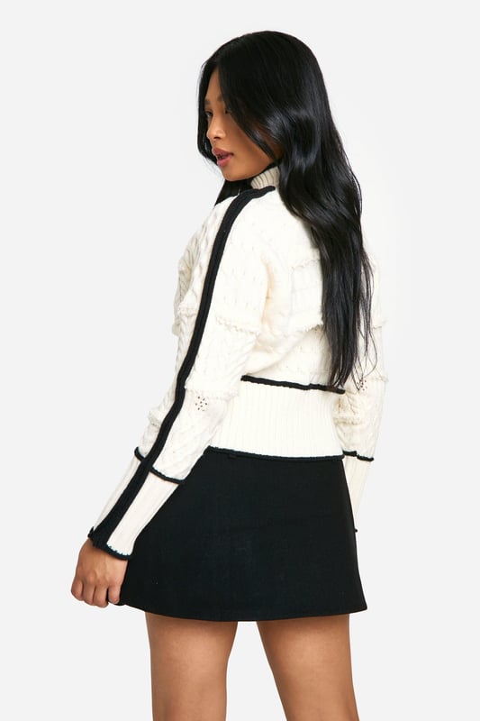 High neck design for a chic, sophisticated look
        Intricate cable knit pattern adds texture and visual interest
        Contrasting trim detail along sleeves and body for a striking effect
        Cropped length perfect for pairing with high-waisted bottoms
        Petite fit tailored for smaller frames
    
    Make a statement in this eye-catching petite cable knit jumper. The high neck design and contrasting trim details create a bold, contemporary look that's perfect for the fashion-forward woman. Style this versatile piece for a range of casual occasions, from coffee dates to family gatherings. Pair it with a high-waisted mini skirt and chunky loafers for a trendy daytime ensemble, or dress it up with tailored trousers and ankle boots for a smart-casual evening look. The cropped length is ideal for showing off your favourite bottoms, while the petite fit ensures a flattering silhouette for smaller frames. Add a leather jacket for extra edge, or keep it simple with minimalist accessories to let the jumper's unique design shine. This Boohoo piece is a must-have addition to your autumn-winter wardrobe, offering both style and comfort for the fashion-conscious woman.