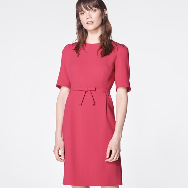 The perfect pink shift, our Elina dress takes its cues from bespoke occasion dresses of an era gone by. Crafted from raspberry pink crepe, it has a round neck, short sleeves, a neat bow belt at the waist and a front panel to the knee-length skirt. Simple and chic, wear it with strappy heels or sleek courts for during the occasion season.