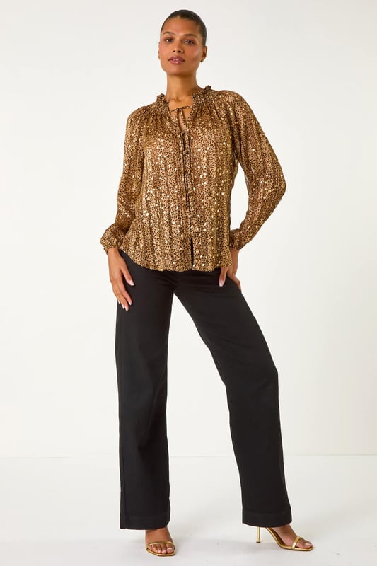 Tie Front Animal Print Blouse from Roman. Embrace your wild side this Autumn/Winter in this stunning animal print blouse. The all over print is elevated with metallic gold spots for a touch of glamour, while the V-Neck and button through front create a chic look. Long sleeves keep you warm, and the tie front detail adds a fun twist to this versatile piece. Pair with pleather trousers and heeled boots for a party ready ensemble that's sure to turn heads!