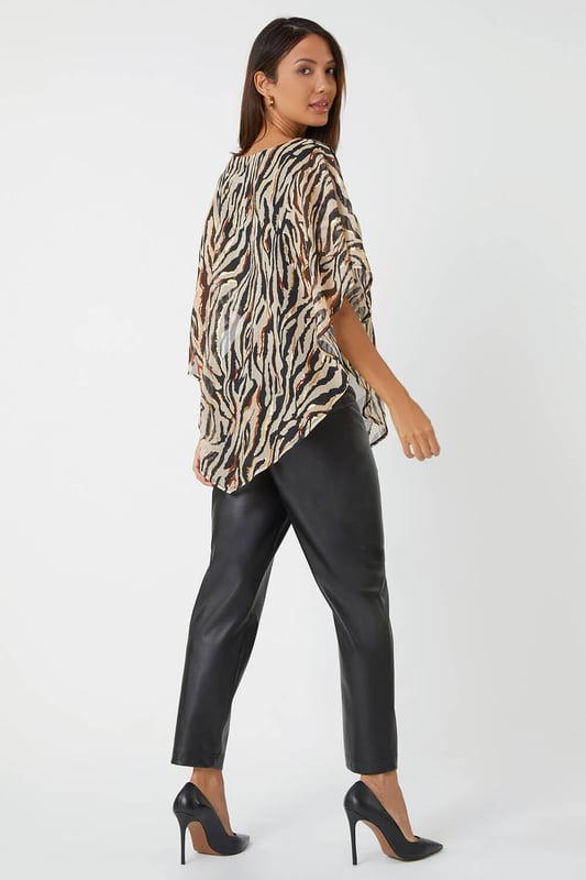 Animal Foil Overlay Stretch Top from Roman. Take a walk on the wild side with this luxurious zebra print party top. Designed with an asymmetrical chiffon overlay that features shimmering foil print, this style is sure to turn heads at your next special occasion. This pull on style has a soft stretch jersey lining for maximum comfort as well as a classic round neckline and short sleeves. Wear with faux leather trousers and heeled boots for style that screams Winter glamour.