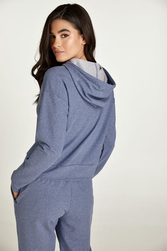Esta sudadera con capucha de color índigo melange está confeccionada en tejido de punto elástico. Una corbata del mismo tejido recorre el interior de la capucha y hay dos topes de metal plateado en los extremos. Hay detalle de costura en los hombros. Tiene manga larga con puño. La sudadera tiene un dobladillo de 7 cm. La prenda tiene un estilo holgado y relajado.