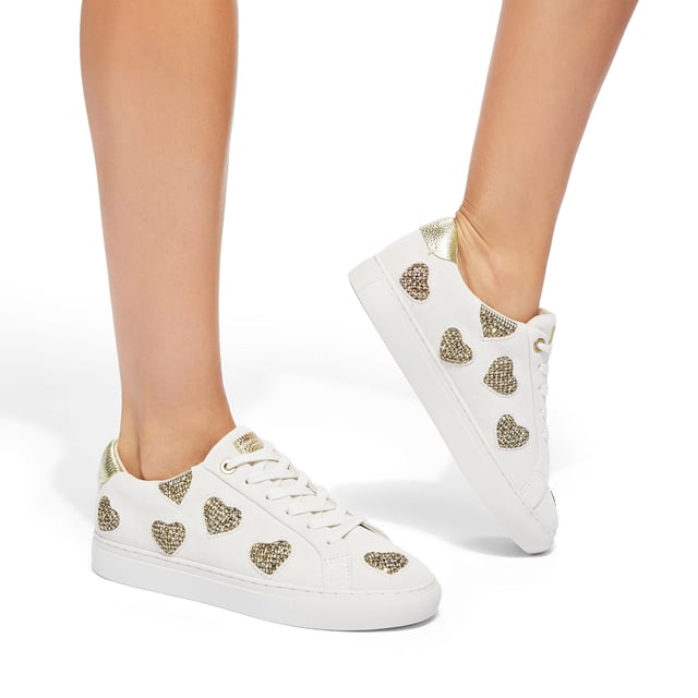 The Kurt Geiger Lane Love sneaker is crafted from a white leather with crystal embellished fabric hearts across the upper. There are two gold leather patches on the tongue and heel with gold foil branding.