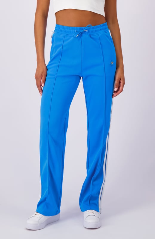 100 % Polyester, ausgestellte Passform, elastischer Bund mit Kordelzug, Reißverschlusstaschen, ikonischer Hexenaufnäher am linken Bein, sportliche Streifen an den Seiten