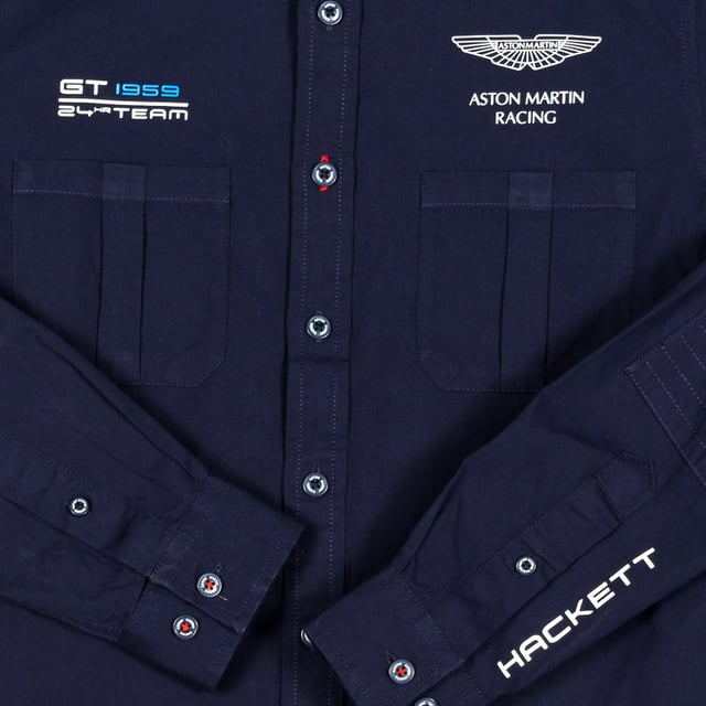 Jongenshemd met lange mouwen van Aston Martin Racing.
 Kraag met kapel.
 Knoopsluiting aan de voorkant.
 Twee open zakken op de voorkant.
 Eigen bedrukking van het merk op de voorkant.
 Gedrukte merknaam op een van de mouwen.
 Manchetten met knoopsluiting.
 Toepassing als elleboogstukken.
 Stoffen label met de vlag van het Verenigd Koninkrijk en de naam van het merk op de onderkant.
 Stoffen label met de merknaam op de achterkant van de hals.
 Naden in toon zichtbaar.
 Samenstelling: 100% katoen
 Onderhoud:
- Maximaal wassen op 30ºC.
 - Strijken op gemiddelde temperatuur, max. 110ºC.
 - Droger is niet toegestaan.
 - Geen bleekmiddel gebruiken.
 - Kan niet chemisch gereinigd worden.