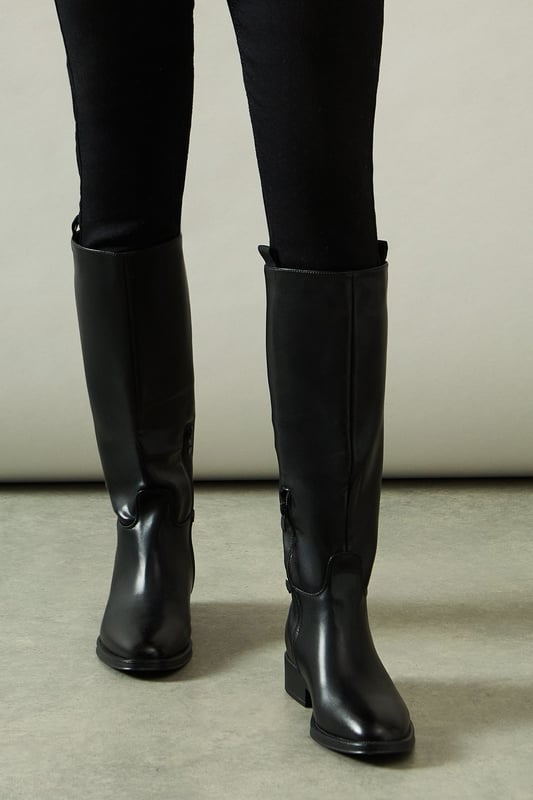 Knee-high riding boot design with sleek silhouette
        Faux leather construction for a polished look
        Distinctive stirrup detail adds equestrian flair
        Low heel measuring between 5 and 6.5cm for comfortable wear
        Side zip closure for easy on and off
    
    Step into sophistication with the Keely Faux Leather Stirrup Detail Low Heel Riding Knee Boot from Wallis. These elegant boots manifest a perfect blend of style and practicality, ideal for the woman who values both comfort and glamour. The knee-high silhouette elongates the leg, while the low heel ensures all-day wearability. Style these versatile boots with skinny jeans and an oversized jumper for a chic daytime look, or pair them with a flowing midi dress for family gatherings. The stirrup detail adds a touch of equestrian charm, making these boots a standout choice for casual outings or countryside walks. Whether you're running errands or meeting friends for brunch, these boots will keep you looking effortlessly stylish and feeling comfortable throughout your day.