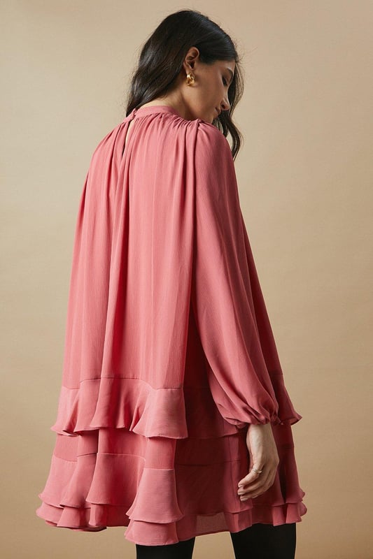 Elegant high neck design for a sophisticated look
        Flowy chiffon fabric creates a graceful silhouette
        Voluminous balloon sleeves add a romantic touch
        Tiered ruffle hem for playful movement
        Versatile mini length suitable for various occasions
    
    This charming high neck chiffon mini dress from Oasis is the epitome of feminine allure. The airy chiffon fabric drapes beautifully, creating a flattering and comfortable fit for all-day wear. The dress features eye-catching balloon sleeves that add a touch of drama to your ensemble, while the tiered ruffle hem introduces a playful element to the overall design. Perfect for casual daytime events, this dress can be styled effortlessly for family gatherings or weekend brunches. Pair it with ankle boots and a leather jacket for an edgy contrast, or opt for ballet flats and delicate jewellery for a softer look. The versatile nature of this dress allows for easy transition from day to night - simply swap your accessories to suit the occasion. Embrace your girly side and make a statement in this delightful Oasis creation.