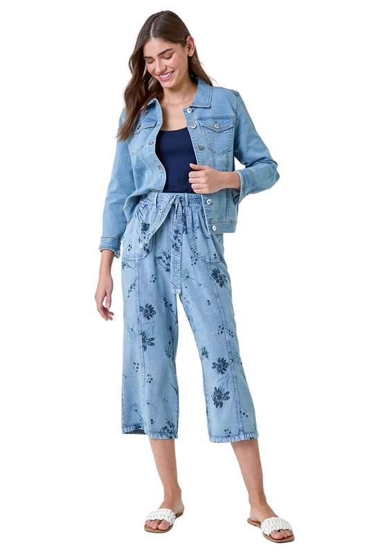 Floral Print Culotte Trousers from Roman. Add a touch of floral flair to your Spring wardrobe with these stylish culotte trousers. Featuring a cute floral print on a denim wash backdrop, these trousers are perfect for the new season. The elasticated waist with a tie belt detail offers both comfort and style, while the cropped culotte length and wide leg shape create a flattering silhouette. The light woven material and pull-on design make them a real Spring staple. Complete your look with a denim jacket, cami top and sandals for effortless daywear.
