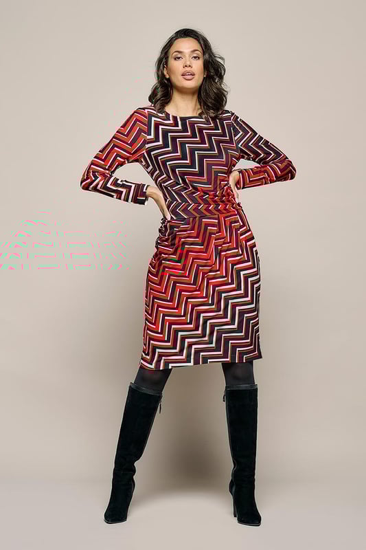 Ontdek de Mart Visser jersey print jurk, genaamd de Eloise. Deze jurk belichaamt stijl en comfort perfect. Het is een echte aanrader vanwege de opvallende contrastrijke print en de kreukvrije jerseykwaliteit die zijdezacht aanvoelt. De stof is bedrukt met een grafische en kleurrijke zigzagprint in rood, wit en zwart, wat een uniek en flatterend effect creëert. De damesjurk biedt heerlijk draagcomfort dankzij de mix van elastaan en polyester, waardoor je je vrij kunt bewegen. De gedrapeerde tailleband flatteert perfect rondom de buik en heupen. Deze knielange jurk heeft een voering met een fijne stretch, sluit met een blinde ritssluiting aan de achterzijde en heeft lange mouwen. Geschikt voor zowel feestelijke als zakelijke gelegenheden. Maak je vrouwelijke en moderne look compleet met een zwart jack en elegante hakken! Ontdek ook de Caitlin print top met dezelfde opvallende print.