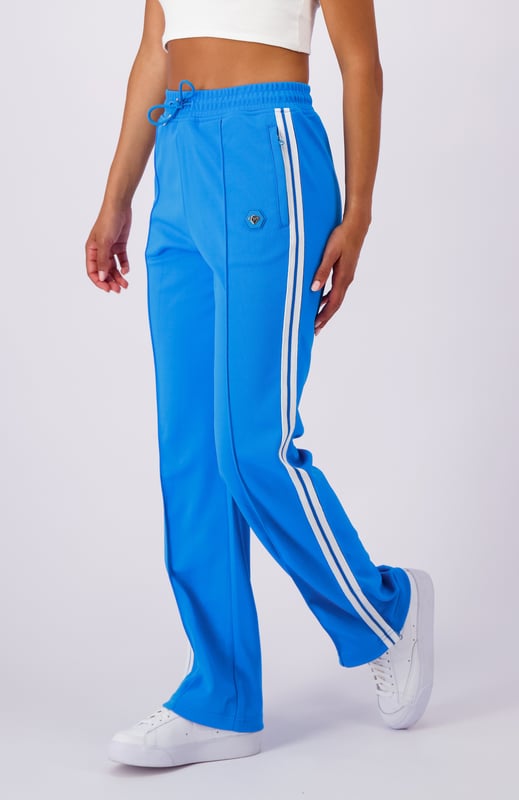 100 % Polyester, ausgestellte Passform, elastischer Bund mit Kordelzug, Reißverschlusstaschen, ikonischer Hexenaufnäher am linken Bein, sportliche Streifen an den Seiten