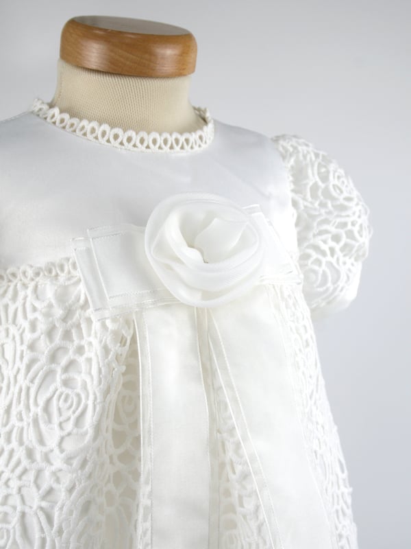 We have reintroduced one of our popular gowns - Ruby. 
  
A stunning Christening robe made with Guipure Lace. A full length dress with a satin bodice, lace sleeves and a beautiful front detail of an organza flower on stunning ribbon tails.  Your child will look very special on the day! 
  
We line our dresses and robes in 100% lightweight Cotton lawn fabric which is cool and better against babies body, especially if they have sensitive skin 
  
The gown arrives to you on a padded Satin hanger and protected by one of our Heritage keepsake garment bags. 
  
Outer - 100% Polyester Mock Silk - Ivory 
Lining - 100% Cotton 
Dry Clean or Hand Wash