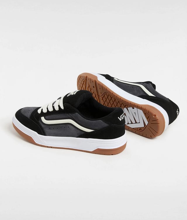 Vans Hylane Schwarze Turnschuhe Tauchen Sie mit Sneakers im Retro-Stil ein, die über Wildleder- und Synthetik-Obermaterialien für Strapazierfähigkeit und Komfort verfügen. Gestaltet mit einer 3D-gelackten Seitenstreife und bestickten Logos für einen kühnen, auffälligen Look. Die klobige Silhouette und die gepolsterte Skater-Zunge vermitteln eine nostalgische Atmosphäre, während die klassische Gummiprofilsohle für zuverlässigen Halt und Traktion sorgt.