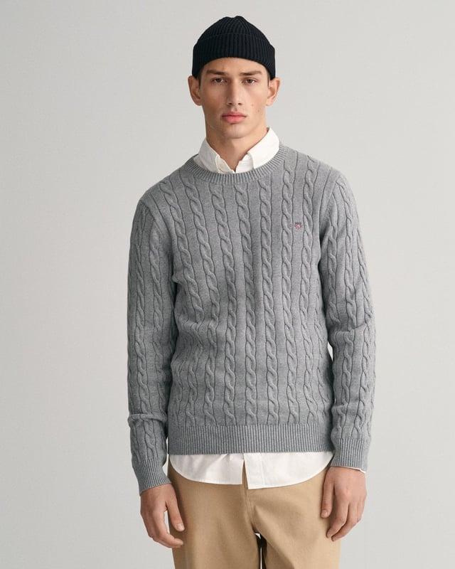 This GANT men's sweater in a traditional cable knit pattern is a stylish addition to any modern wardrobe. With its classic crew neck and ribbed trims, it offers a comfortable fit, while the embroidered GANT crest graphic on the chest provides a sophisticated accent. It pairs perfectly with jeans or pants.