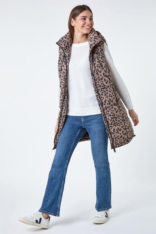Animal Print Longline Hooded Gilet from Roman. Gilets are the perfect option for the transitional seasons, providing just the right amount of warmth for unpredictable weather. Cut from a woven fabric this gilet features a cosy funnel neck and a front zip fastening for a secure fit. A practical hood is finished with a drawstring cord for an adjustable fit, while zipped pockets provide space for your everyday essentials. Adorned in a fun animal print this piece is padded for extra warmth. Pair with relaxed denim and knitwear with either boots and trainers for trendy everyday style!